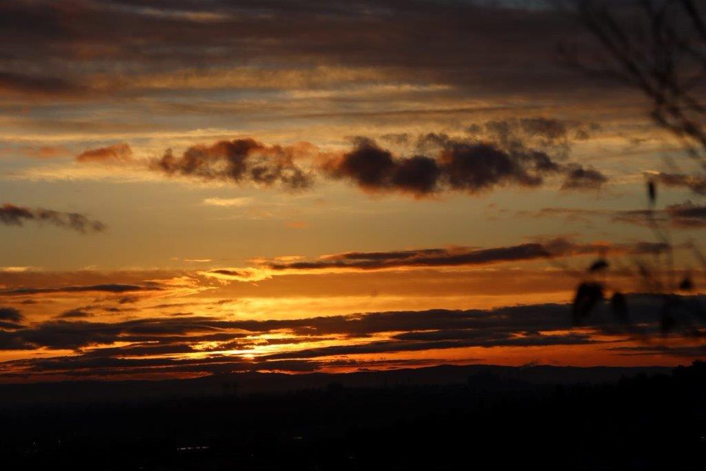 A sunset with clouds and a person flying a kite

Description automatically generated