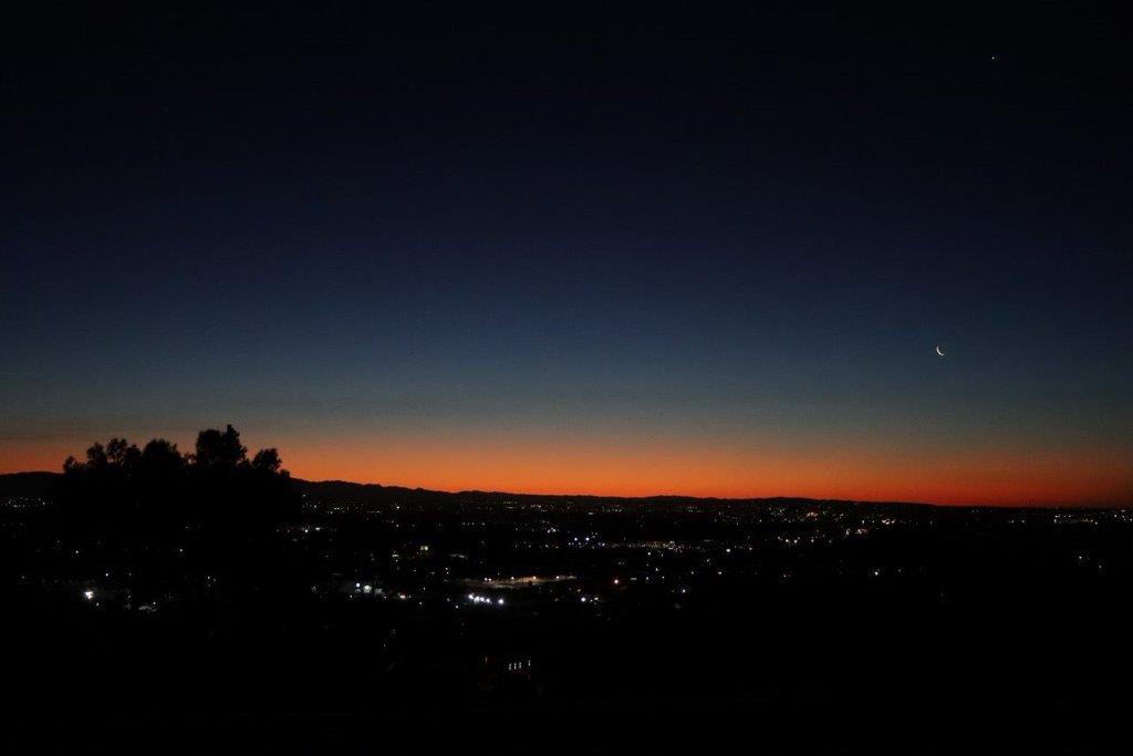 A city at night with a bright orange sky

Description automatically generated