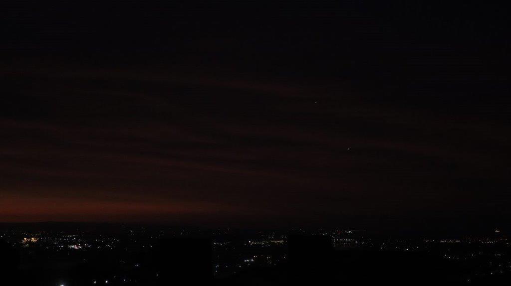A city at night with a light in the sky

Description automatically generated