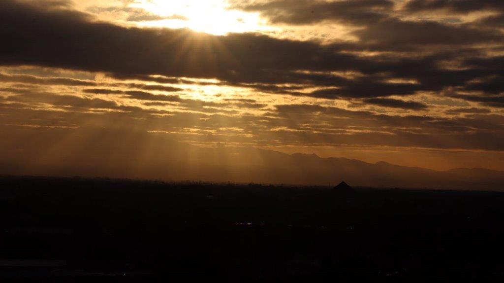 Sun shining through clouds over a desert

Description automatically generated