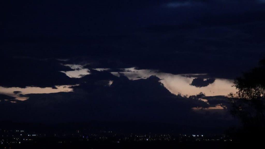 A dark sky with clouds and a city at night

Description automatically generated