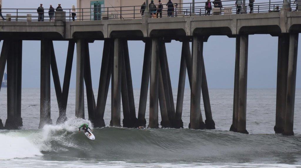 A person surfing under a pier

Description automatically generated
